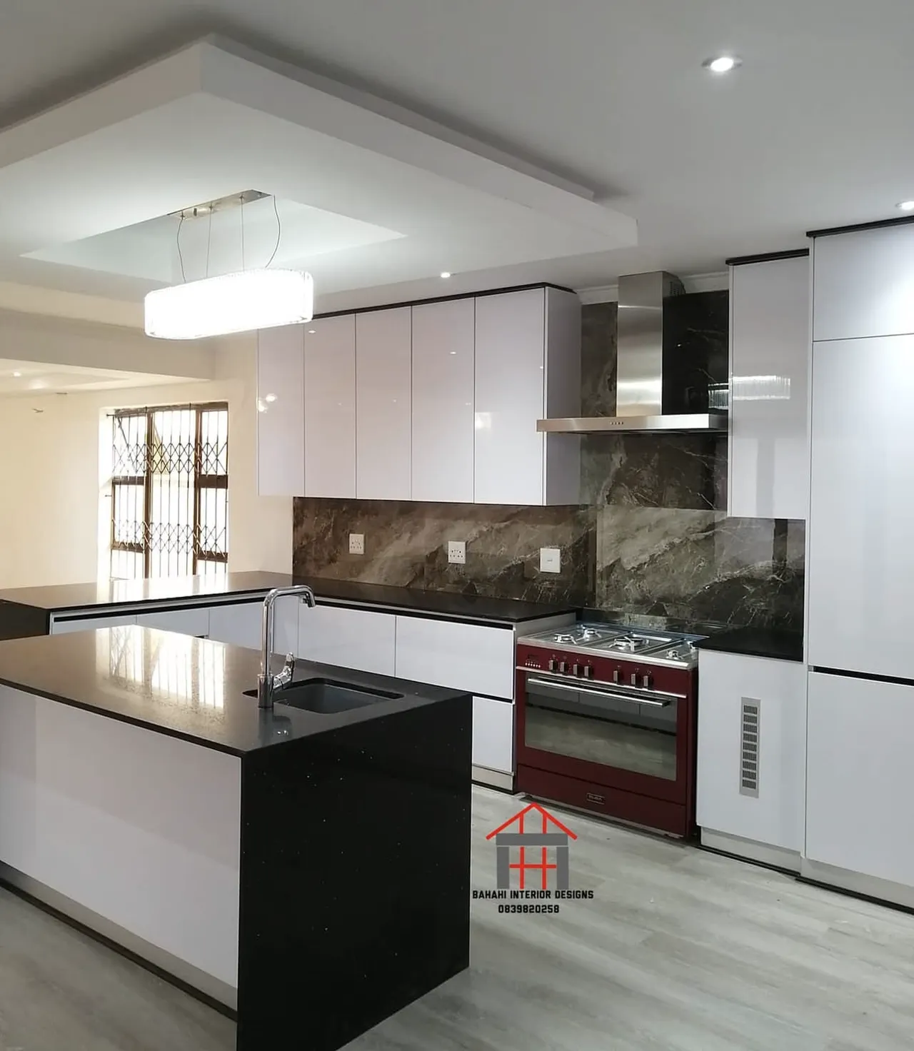 An iceberg white gloss kitchen trimmed in black, with two black waterfall islands, a marble-look splashback and a red range cooker.