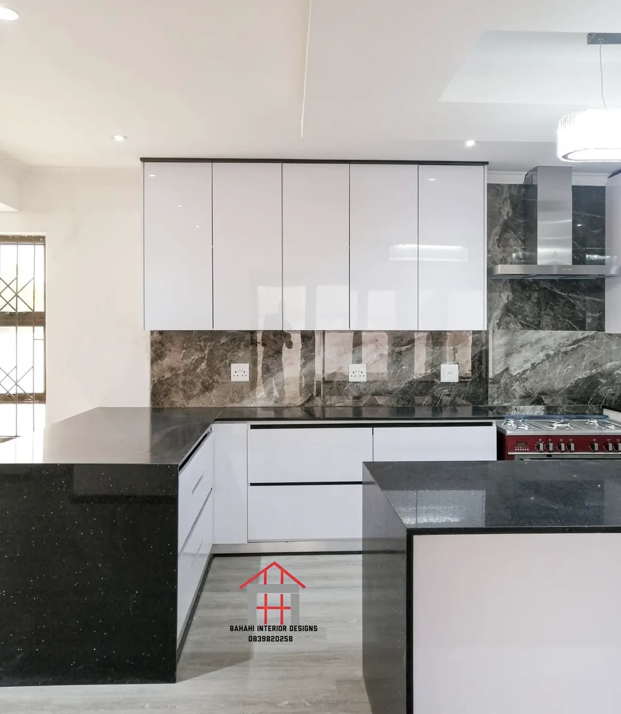 Handleless white gloss wall cupboards over a dark marble-look splashback and black stone tops.