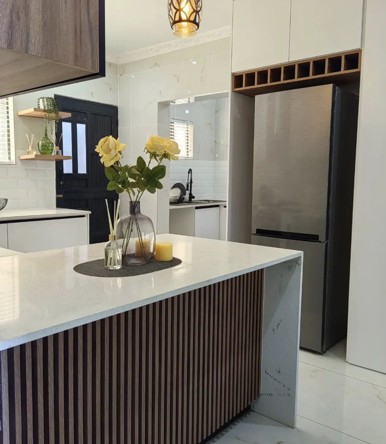 A slatted peninsula in front of a fridge housed in white units with a timber wine rack above.