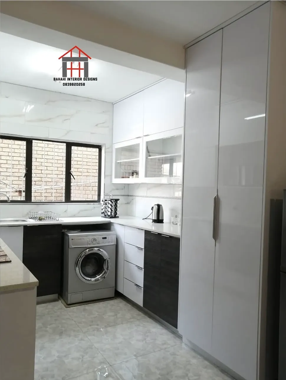 A tall white gloss unit beside a white and dark oak kitchen with a washing machine space under the counter.