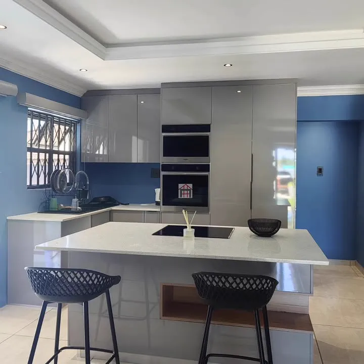 A grey high-gloss kitchen with a stone-topped island, two built-in ovens and blue walls.
