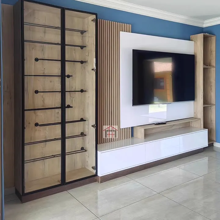 A white gloss TV wall with timber slats beside a tall black-framed glass cabinet.
