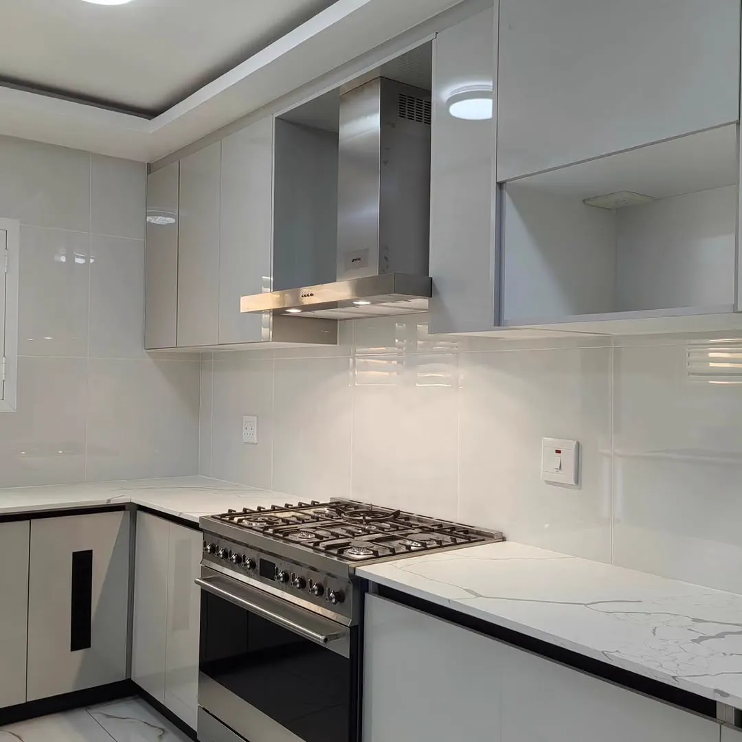 A six-burner gas range under a steel hood, between light gloss cupboards and a calacatta top.