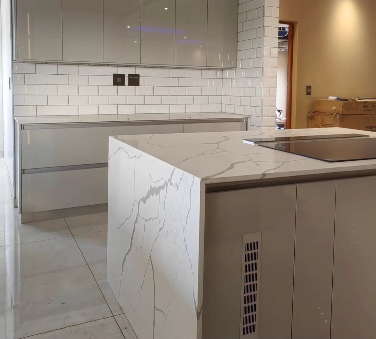 A waterfall island in veined white stone in front of grey gloss cupboards and white subway tiles.