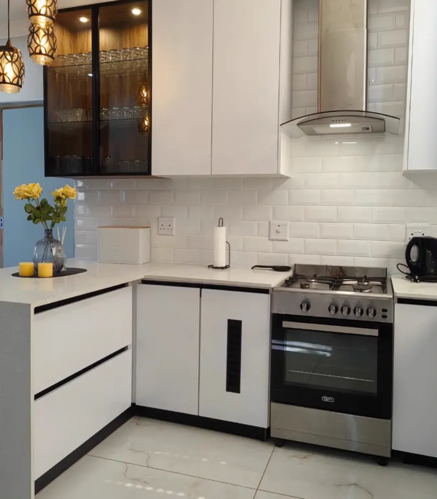 A black-framed glass cabinet of glasses above white cupboards with black channel handles.
