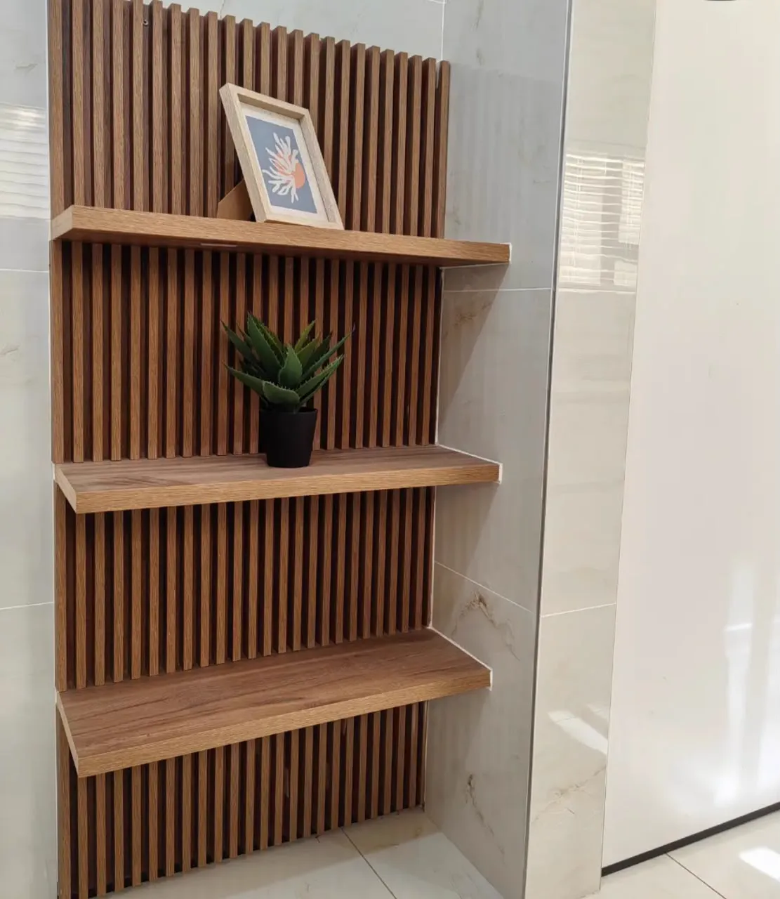 Three timber shelves on a slatted wall panel, holding a framed print and an aloe.