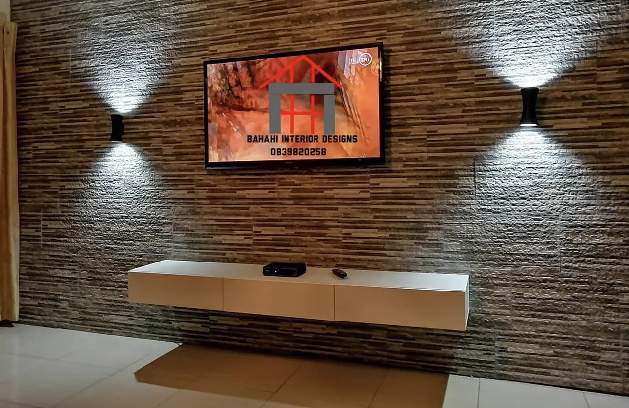 A TV wall clad in textured stone-look tiles, with two wall lights and a floating white cabinet.