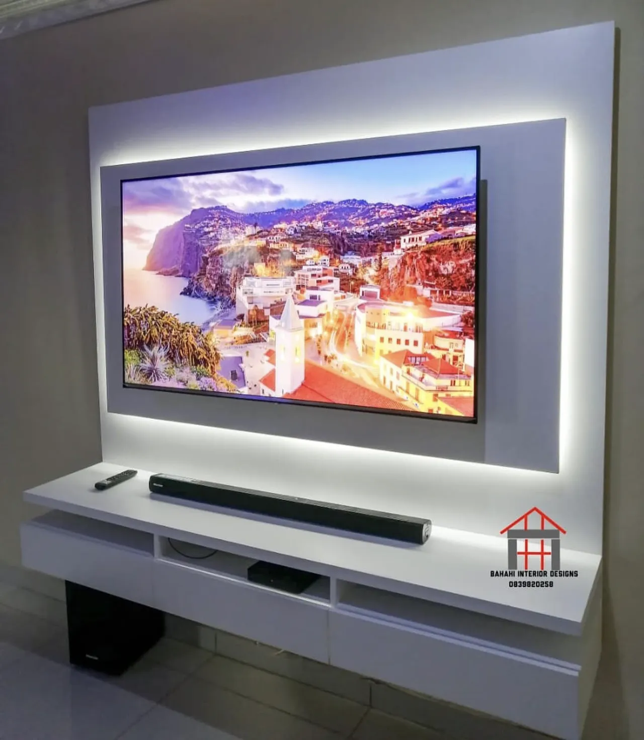 A white wall-mounted TV stand with a raised panel behind the screen, lit around its edge.