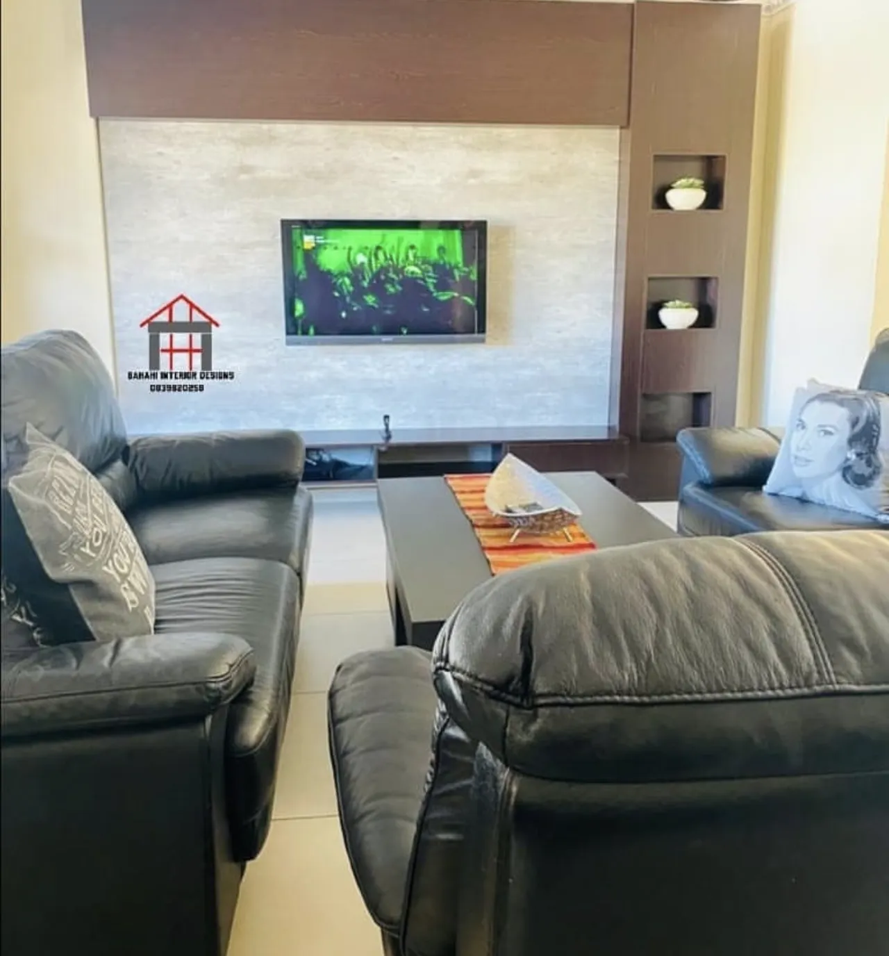 The wenge and stone TV wall seen from the lounge, behind black leather sofas.