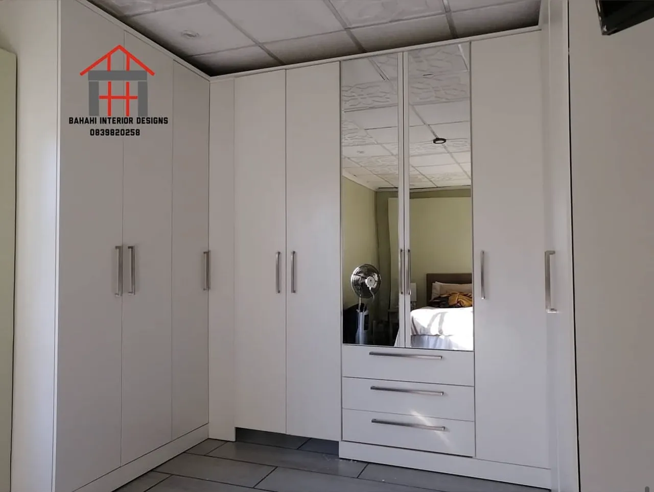 A white three-wall walk-in cupboard with two mirrored doors and a bank of drawers.