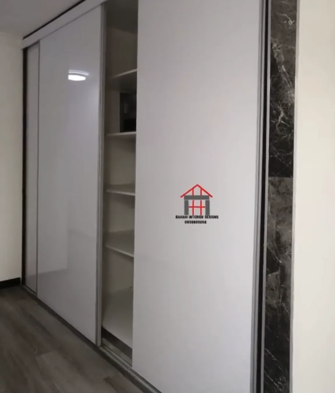 A full-height white gloss storage cabinet with sliding doors and shelving inside.